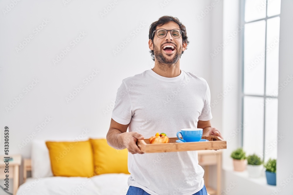 Handsome latin man eating breakfast on the bed smiling and laughing hard out loud because funny crazy joke. Handsome latin man eating breakfast on the bed smiling and laughing hard out loud because funny crazy joke.