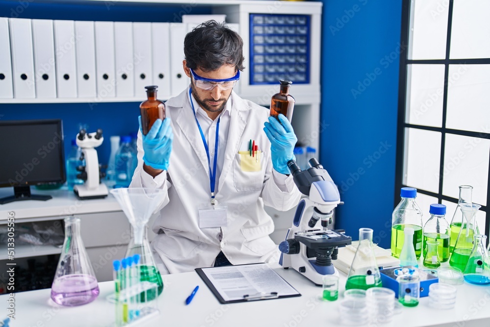 Young hispanic man scientist holding bottles at laboratory Young hispanic man scientist holding bottles at laboratory