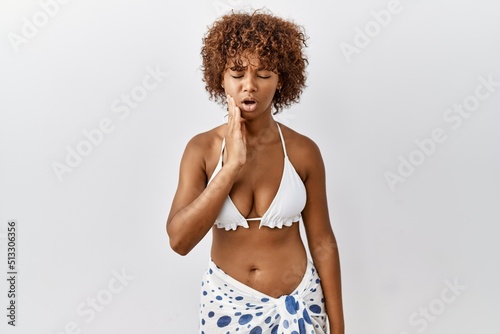 Young african american woman with curly hair wearing bikini touching mouth with hand with painful expression because of toothache or dental illness on teeth. dentist