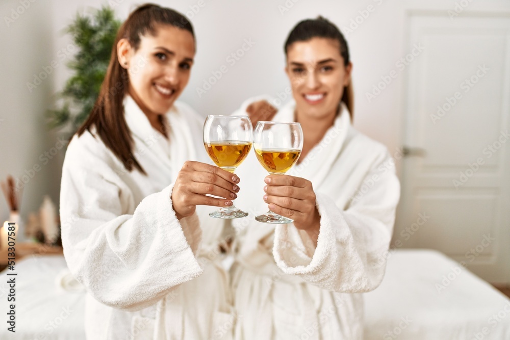Two women wearing bathrobe toasting with champagne standing at beauty center Two women wearing bathrobe toasting with champagne standing at beauty center