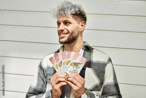 Young hispanic man smiling happy holding new zealand dollars at the city. photo