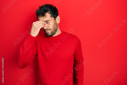 Handsome man with beard wearing casual red sweater tired rubbing nose and eyes feeling fatigue and headache. stress and frustration concept.