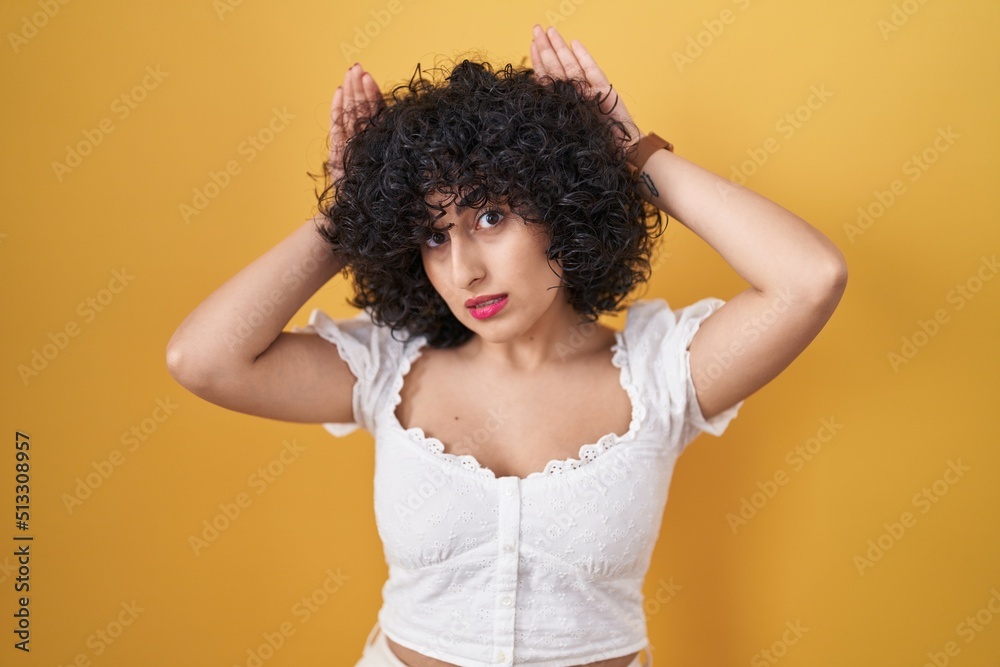 Young brunette woman with curly hair standing over yellow background doing bunny ears gesture with hands palms looking cynical and skeptical. easter rabbit concept. Young brunette woman with curly hair standing over yellow background doing bunny ears gesture with hands palms looking cynical and skeptical. easter rabbit concept.