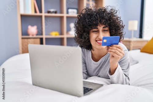 Young middle east woman using laptop and credit card lying on bed at bedroom