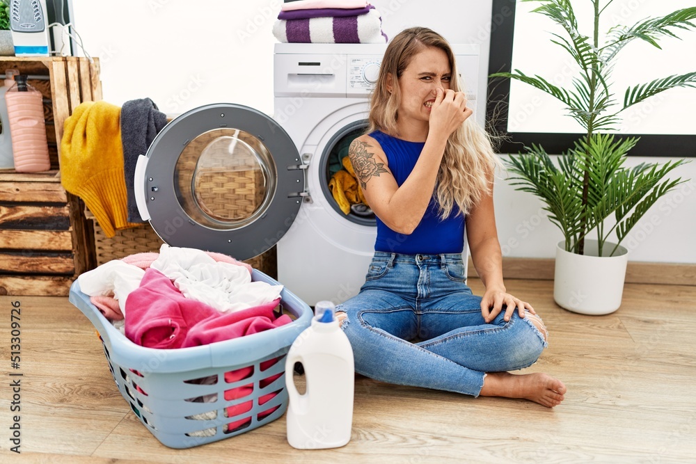 Young beautiful woman doing laundry sitting by wicker basket smelling