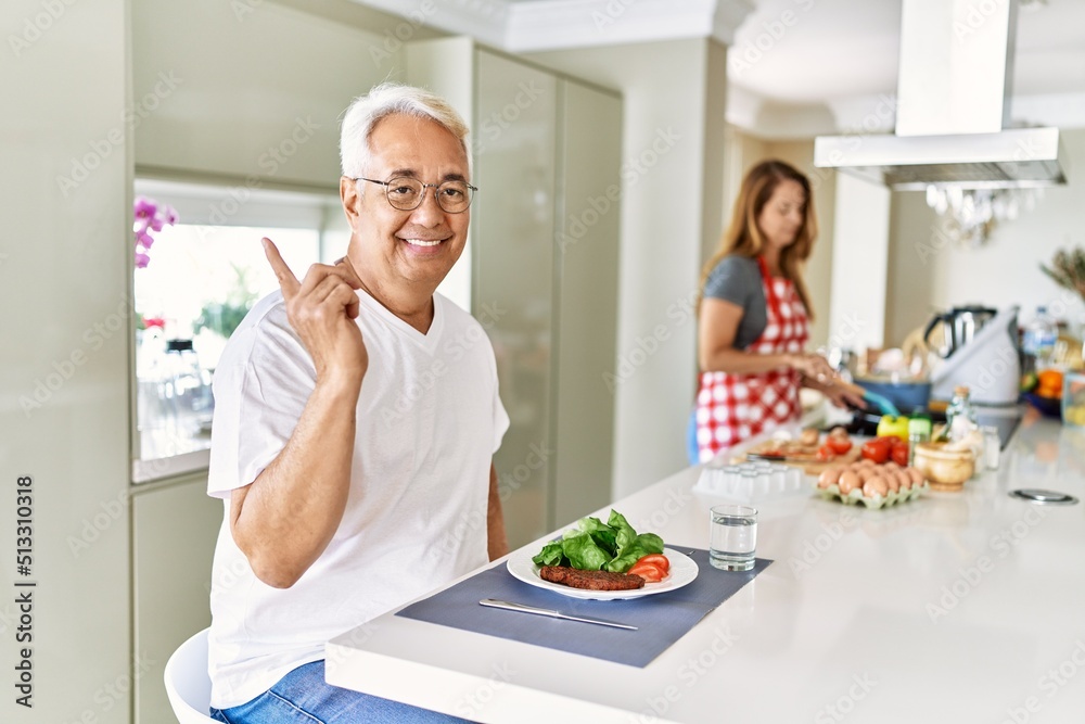 Middle age hispanic couple eating healthy meal at home smiling happy pointing with hand and finger to the side Middle age hispanic couple eating healthy meal at home smiling happy pointing with hand and finger to the side