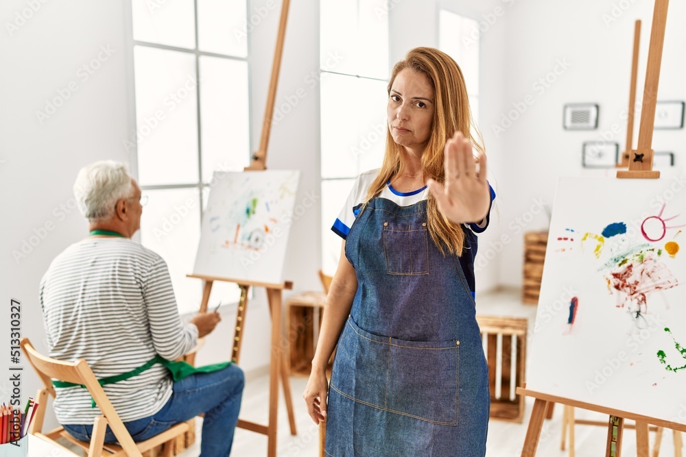 Hispanic woman wearing apron at art studio doing stop sing with palm of the hand. warning expression with negative and serious gesture on the face.