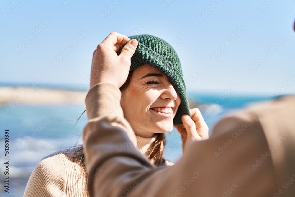 Mand and woman couple smiling confident put cap on head at seaside