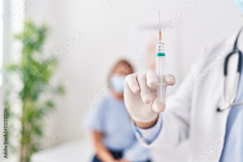 Middle age man and woman doctor and patient holding syringe at clinic