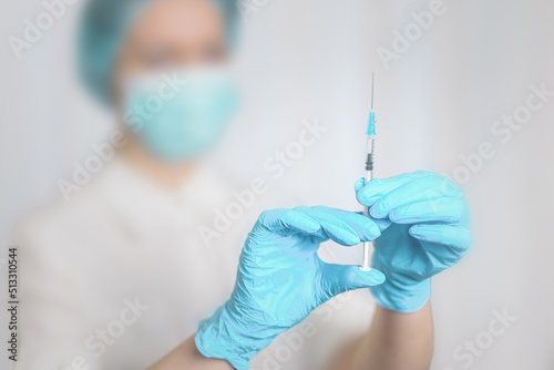 hands of a female doctor in blue nitrile gloves for protection holds a syringe for injection. selective focus.