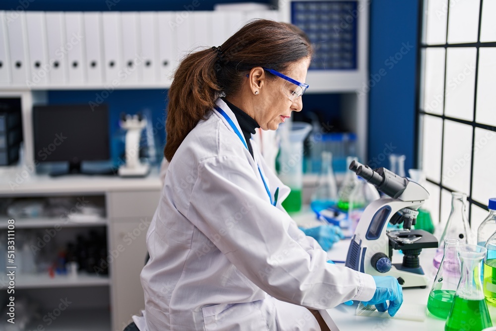 Middle age man and woman scientists using microscope working at laboratory Middle age man and woman scientists using microscope working at laboratory