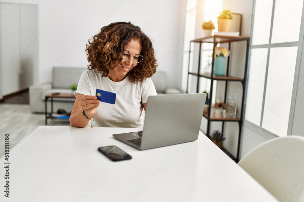 Middle age hispanic woman using laptop holding credit card at home Middle age hispanic woman using laptop holding credit card at home