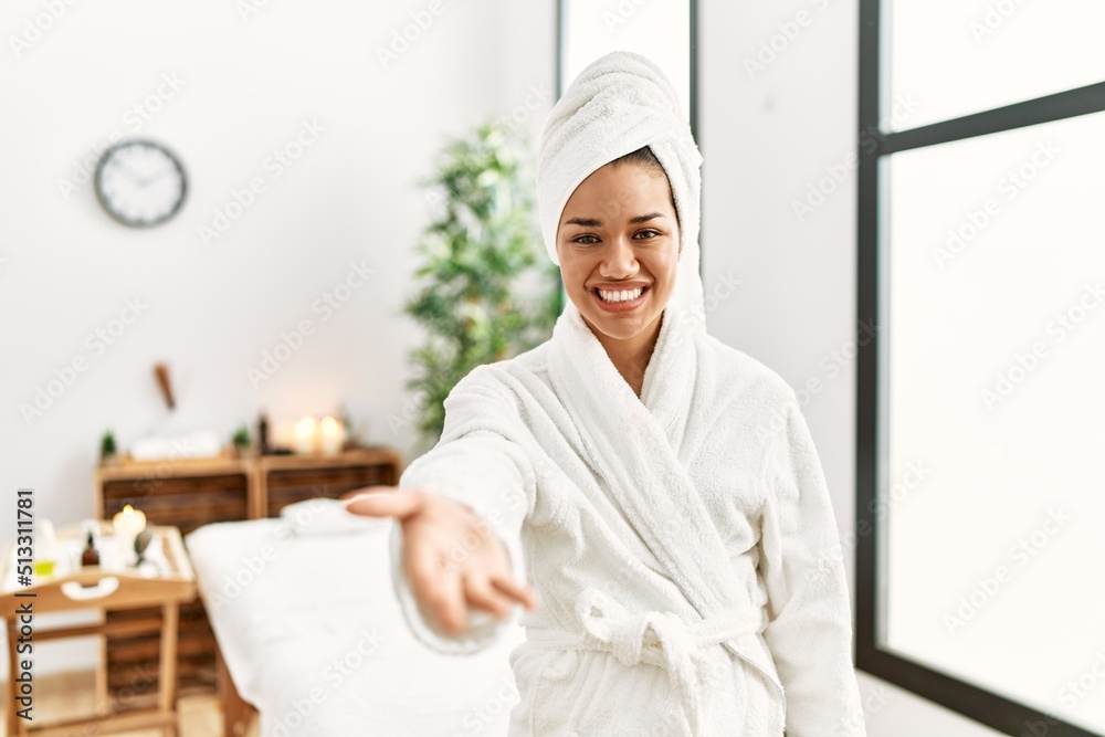 Young brunette woman wearing towel and bathrobe standing at beauty center smiling friendly offering handshake as greeting and welcoming. successful business. Young brunette woman wearing towel and bathrobe standing at beauty center smiling friendly offering handshake as greeting and welcoming. successful business.
