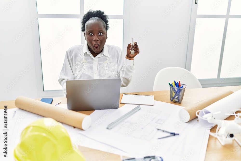 Young african woman working at architecture studio holding house keys scared and amazed with open mouth for surprise, disbelief face