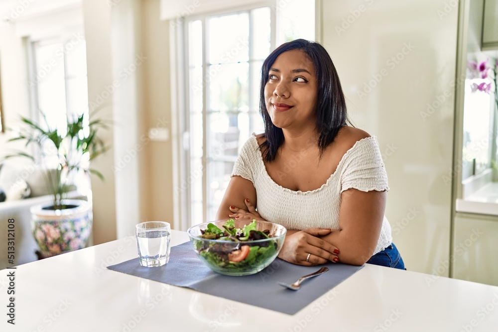 Young hispanic woman eating healthy salad at home smiling looking to the side and staring away thinking. Young hispanic woman eating healthy salad at home smiling looking to the side and staring away thinking.