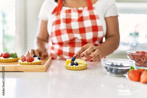 Hispanic brunette woman preparing pastries with fruits at the kitchen