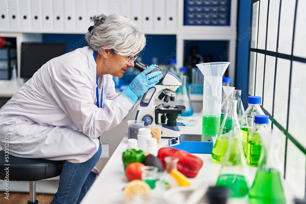 Middle age woman wearing scientist uniform using microscope at laboratory