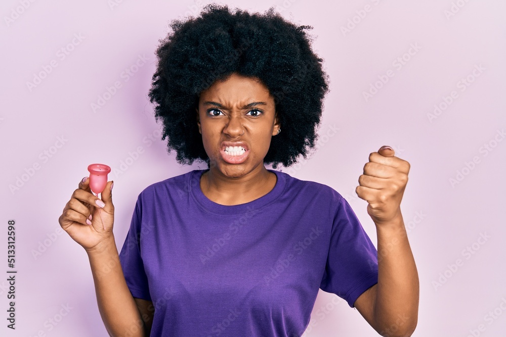Young african american woman holding menstrual cup annoyed and frustrated shouting with anger, yelling crazy with anger and hand raised Young african american woman holding menstrual cup annoyed and frustrated shouting with anger, yelling crazy with anger and hand raised