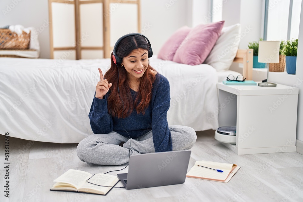 Hispanic young woman using laptop sitting on the floor at the bedroom ...