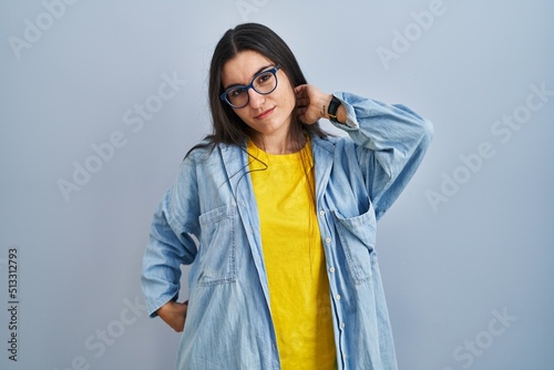 Young hispanic woman standing over blue background suffering of neck ache injury, touching neck with hand, muscular pain
