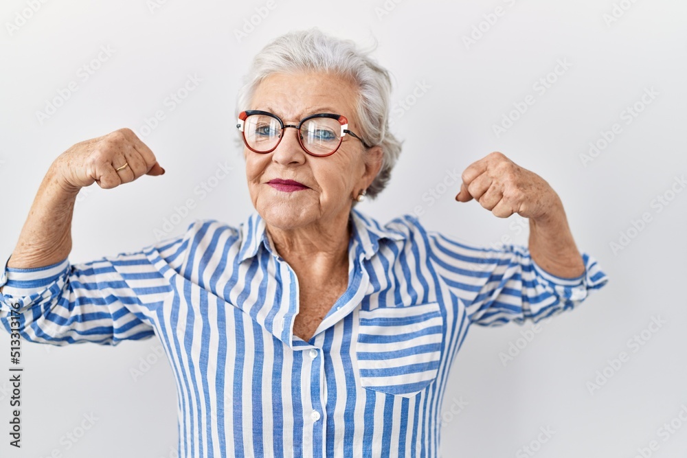 Senior woman with grey hair standing over white background showing arms muscles smiling proud. fitness concept. Senior woman with grey hair standing over white background showing arms muscles smiling proud. fitness concept.