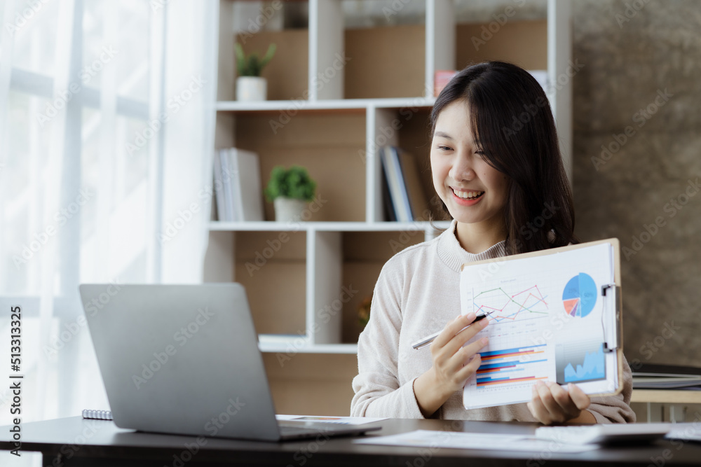 Beautiful Asian businesswoman sitting in her private office, she is talking to her partner via video call on her laptop, she is a female executive of a startup company. Concept of financial management
