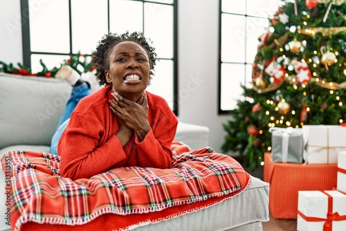 Young african american woman lying on the sofa by christmas tree shouting and suffocate because painful strangle. health problem. asphyxiate and suicide concept.