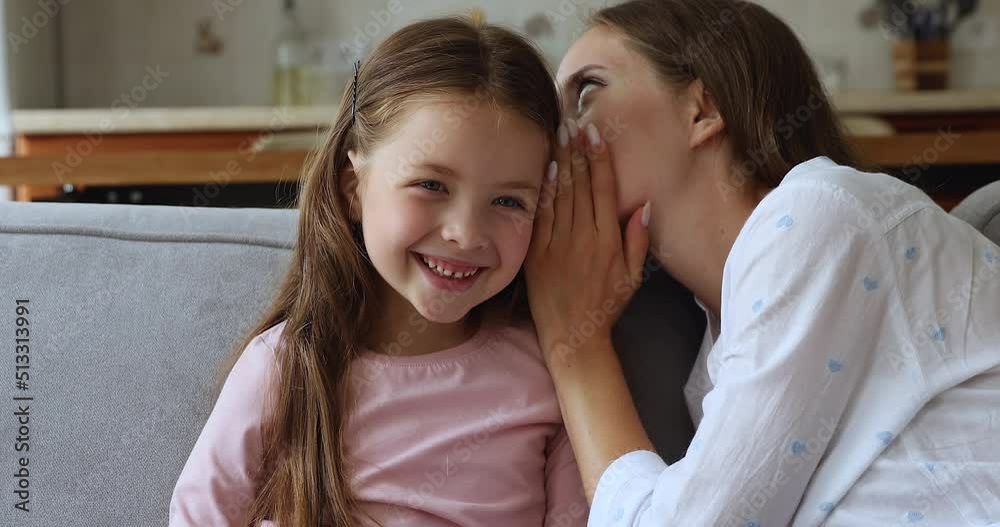 Cheerful loving mom whispering in little daughters ear, telling secret with joyful giggling laughing kid. Young mother telling funny story, joke to child, enjoying friendship, trust, motherhood Cheerful loving mom whispering in little daughters ear, telling secret with joyful giggling laughing kid. Young mother telling funny story, joke to child, enjoying friendship, trust, motherhood