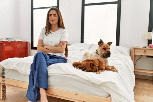 Photography Young brunette woman sitting on the bed with two dogs skeptic and nervous, disapproving expression on face with crossed arms