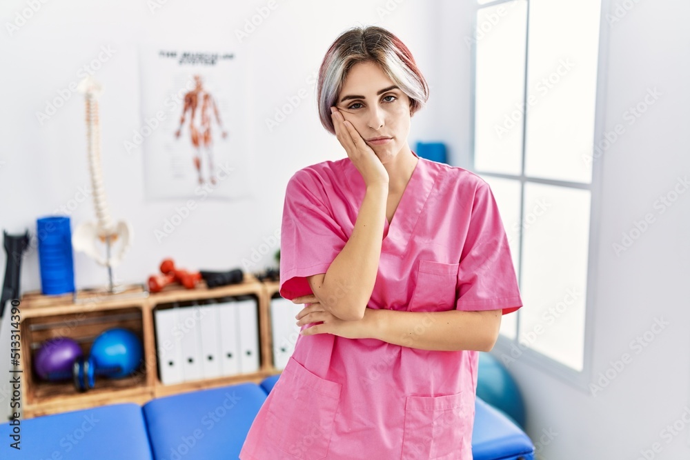 Young nurse woman working at pain recovery clinic thinking looking tired and bored with depression problems with crossed arms.