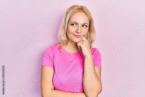 Young blonde woman wearing casual pink t shirt thinking concentrated about doubt with finger on chin and looking up wondering