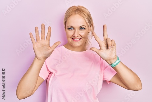 Young blonde woman wearing casual pink t shirt showing and pointing up with fingers number eight while smiling confident and happy.