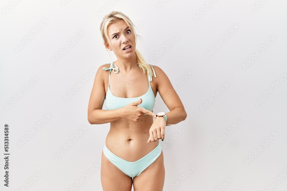 Fototapeta premium Young caucasian woman wearing bikini over isolated background in hurry pointing to watch time, impatience, upset and angry for deadline delay