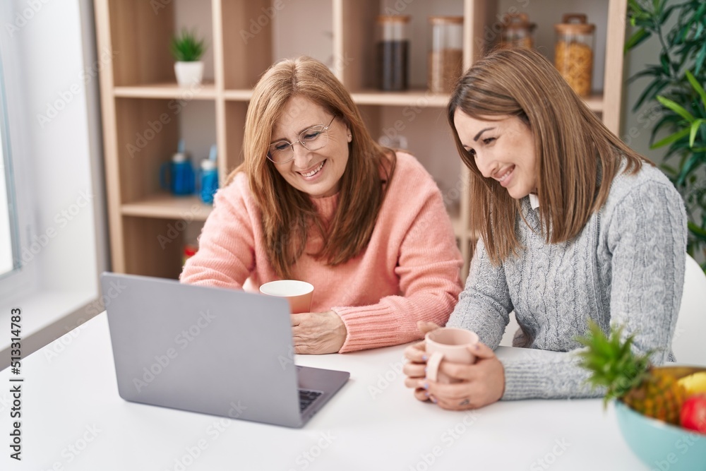 Mother and daughter drinking coffee using laptop at home Mother and daughter drinking coffee using laptop at home