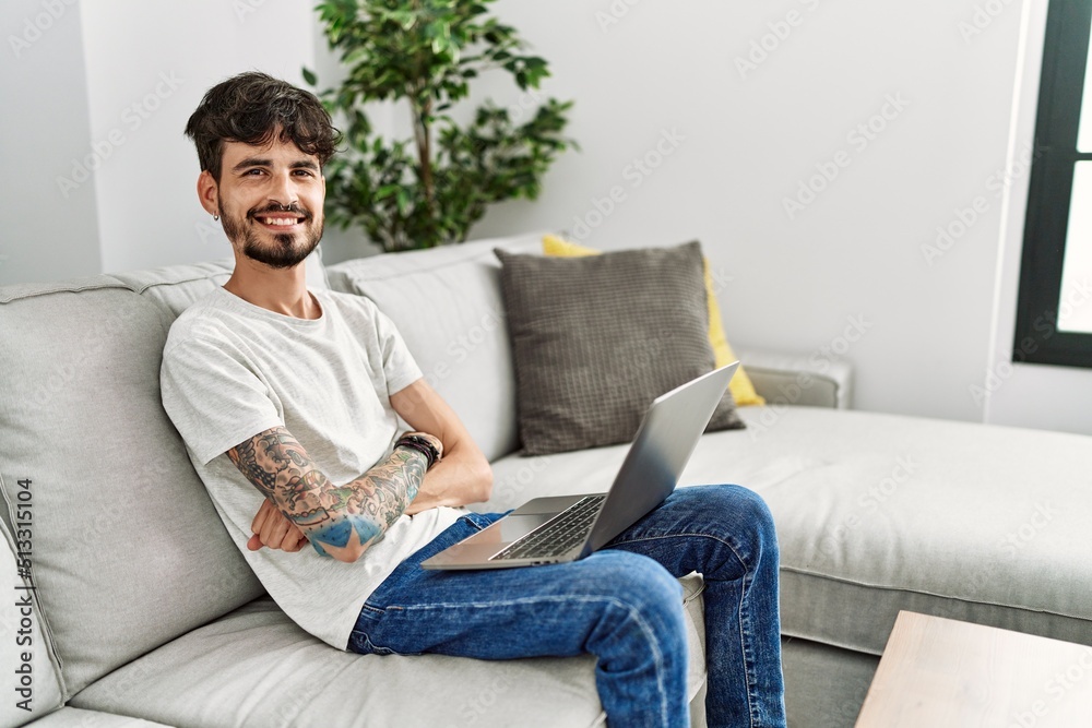 Hispanic man with beard sitting on the sofa happy face smiling with crossed arms looking at the camera. positive person.
