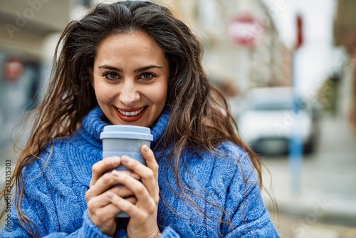 Young hispanic woman smiling happy smelling coffee at the city.