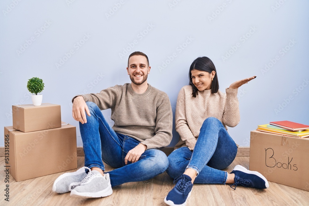 Young couple moving to a new home smiling cheerful presenting and pointing with palm of hand looking at the camera. Young couple moving to a new home smiling cheerful presenting and pointing with palm of hand looking at the camera.