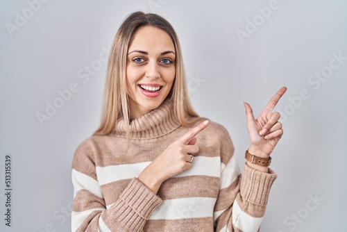 Young blonde woman wearing turtleneck sweater over isolated background smiling and looking at the camera pointing with two hands and fingers to the side.