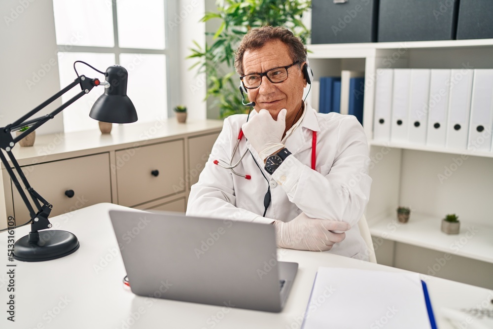 Senior doctor man working on online appointment looking confident at the camera smiling with crossed arms and hand raised on chin. thinking positive.
