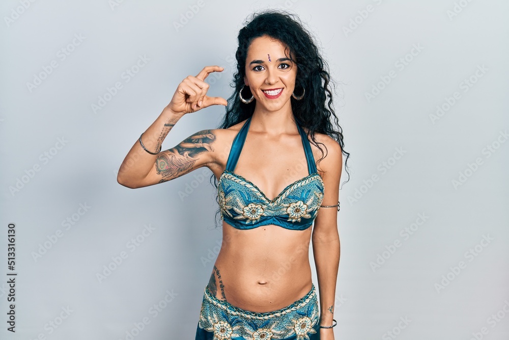 Fototapeta premium Young woman wearing bindi and traditional belly dance clothes smiling and confident gesturing with hand doing small size sign with fingers looking and the camera. measure concept.