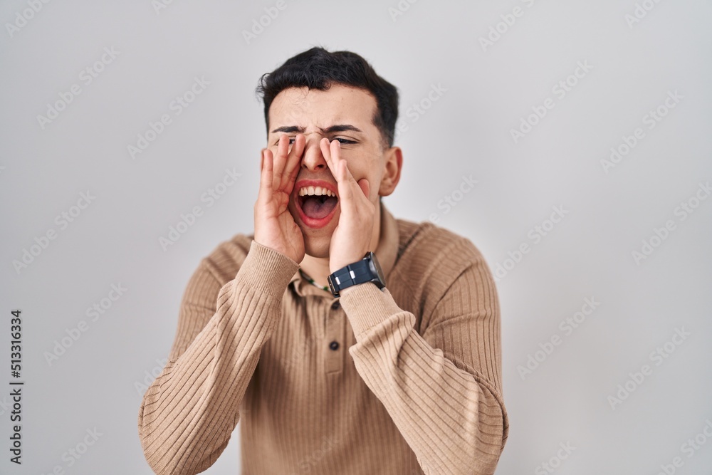 Non binary person standing over isolated background shouting angry out loud with hands over mouth Non binary person standing over isolated background shouting angry out loud with hands over mouth