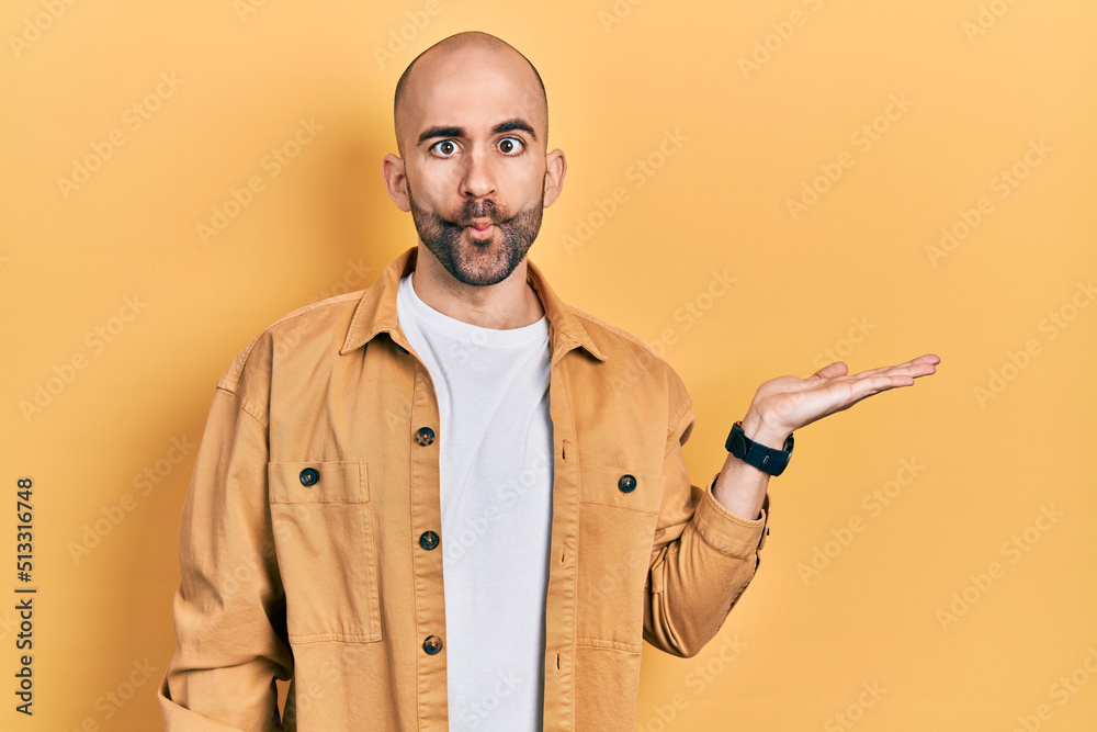 Young bald man presenting with open palms, holding something making fish face with mouth and squinting eyes, crazy and comical. Young bald man presenting with open palms, holding something making fish face with mouth and squinting eyes, crazy and comical.