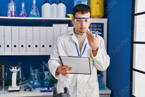 Young man scientist talking on the smartphone reading document at laboratory