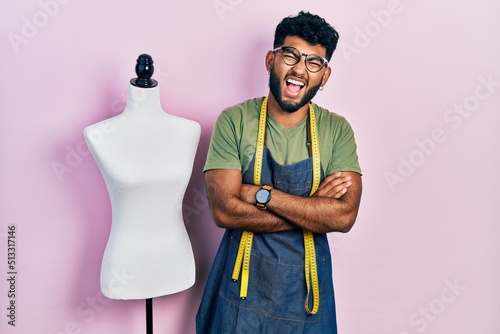 Arab man with beard dressmaker designer wearing atelier apron smiling and laughing hard out loud because funny crazy joke.
