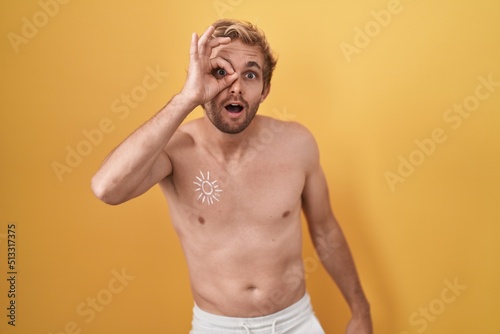 Caucasian man standing shirtless wearing sun screen doing ok gesture shocked with surprised face, eye looking through fingers. unbelieving expression.