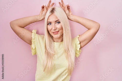Caucasian woman standing over pink background posing funny and crazy with fingers on head as bunny ears, smiling cheerful