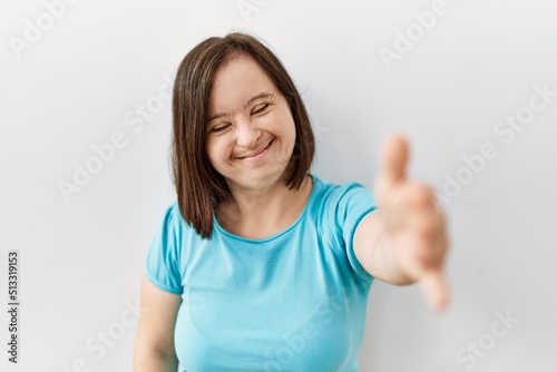 Young down syndrome woman standing over isolated background smiling friendly offering handshake as greeting and welcoming. successful business.