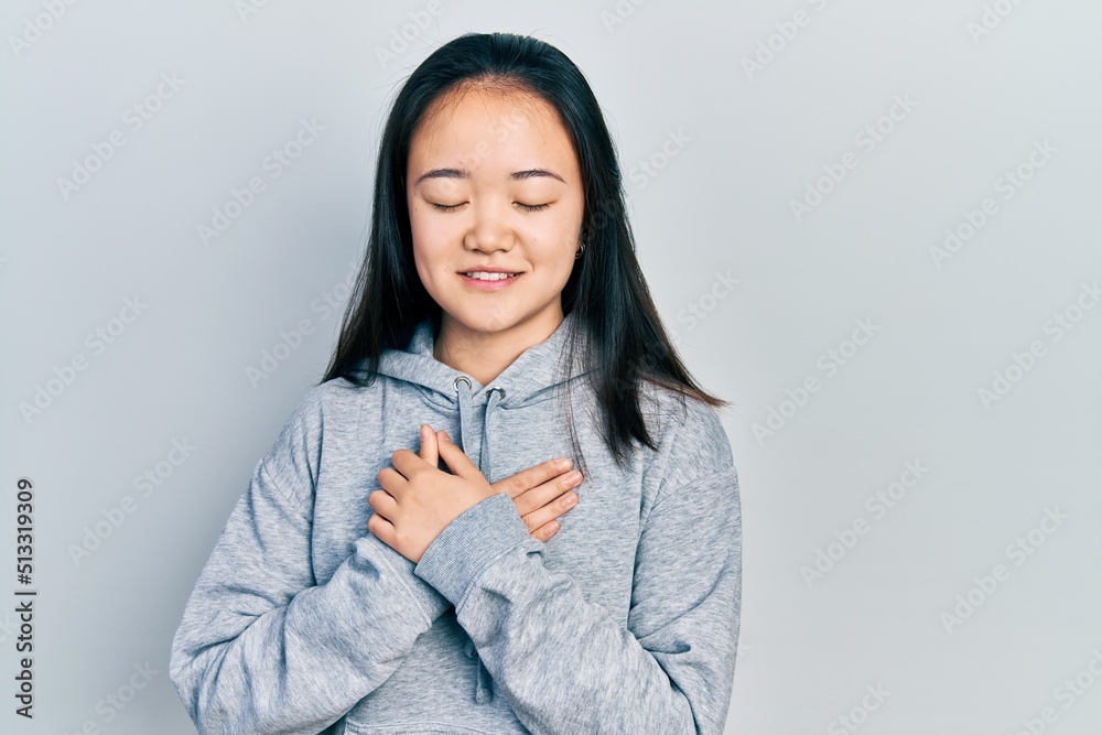 Young chinese girl wearing casual clothes smiling with hands on chest with closed eyes and grateful gesture on face. health concept. Young chinese girl wearing casual clothes smiling with hands on chest with closed eyes and grateful gesture on face. health concept.