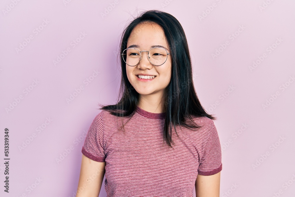 Young chinese girl wearing casual clothes and glasses looking away to side with smile on face, natural expression. laughing confident. Young chinese girl wearing casual clothes and glasses looking away to side with smile on face, natural expression. laughing confident.