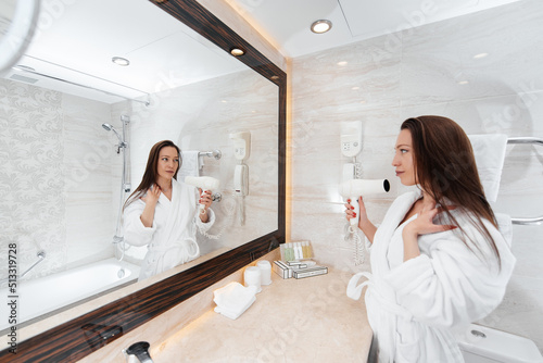 A young beautiful girl is drying her hair in a beautiful white bathroom. A fresh good morning at the hotel. Rest and travel. Hotel recreation, and tourism.